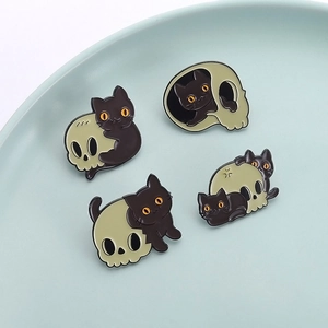 Creative black cat and skull enamel pin badges displayed on a decorative ceramic tray