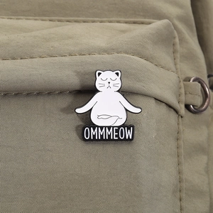 Détail d'un pin's en émail chat de yoga avec texte OMMMEOW sur un sac en toile verte