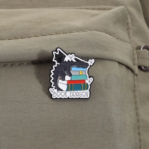 Gros plan d'un badge émaillé de dragon avec texte BOOK DRAGON attaché sur un sac vert olive
