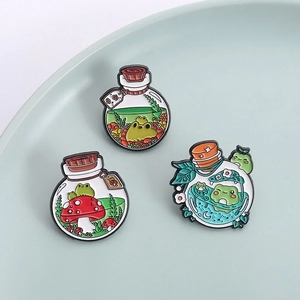 Three enamel pins featuring cute frogs and mushrooms in magic bottles on a blue ceramic dish