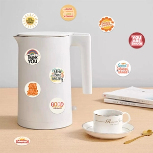 Self-adhesive motivational phrase stickers on a white kettle with cozy home decor background