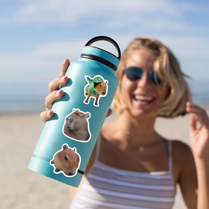 Three realistic capybara stickers shown on a blue water bottle with a beach background