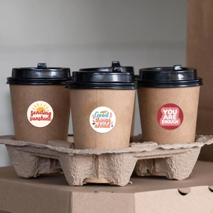 Close-up of sending sunshine and good things ahead round stickers on coffee cups