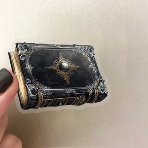 Nahaufnahme eines Vintage-Zauberbuch-Aufklebers mit Golddetails in der Hand