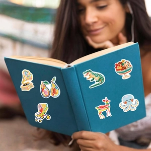 Gros plan d'autocollants de dessins animés colorés décorant un livre bleu tenu par une fille