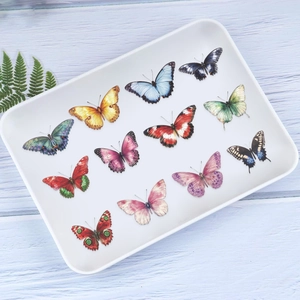 Vue détaillée de 11 autocollants papillons colorés sur un plateau avec feuille verte