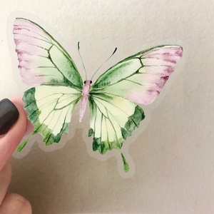 Vue rapprochée d'un autocollant papillon aquarelle rose et vert tenu par les doigts
