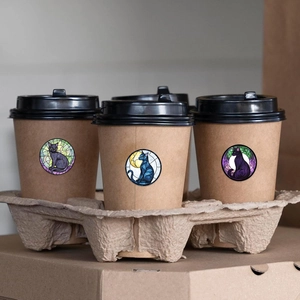 Cat and moon stained glass stickers displayed on coffee cups in a warm cafe setting