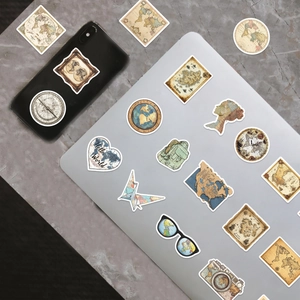 Detail of vintage travel stickers featuring world maps and compass on laptop and phone