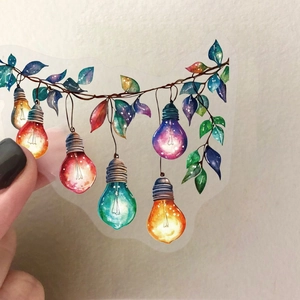 Close-up of a hand holding a transparent PET sticker with colorful light bulb patterns