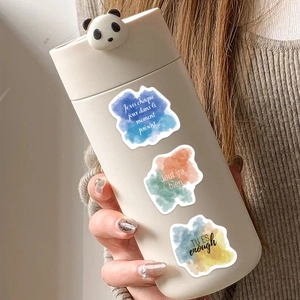 Close-up of motivational watercolor stickers with French text on a cream panda coffee cup