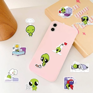 Detail of cute green alien stickers on a smartphone and book for aesthetic DIY decoration