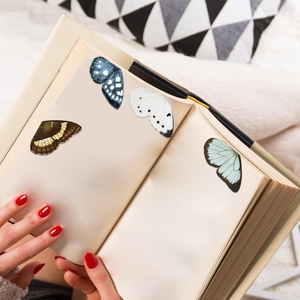 Detalle de cuatro marcapáginas magnéticos de mariposas de colores en la página de un libro