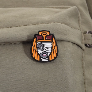 Macro detail of Cleo de Nile enamel pin on olive green fabric with vivid orange hair and bandage