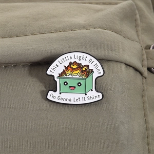 Detail of enamel pin with burning dumpster and text on olive green fabric strap