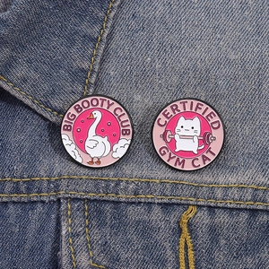 Lustiges Anstecknadel-Set mit Schwan und Gym-Katze Motiven auf einer blauen Jeansjacke