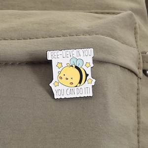 Detail of cute enamel bee pin with motivational quotes on khaki fabric background