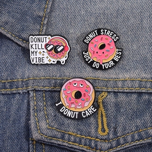 Tre spille creative in smalto a forma di ciambella rosa su una giacca di jeans blu
