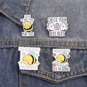 Detail of four cute bee enamel pins on blue denim jacket with motivational puns