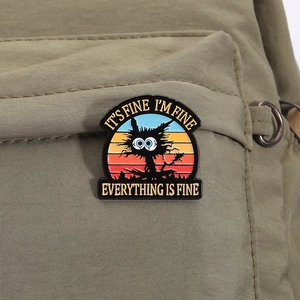 Detail of funny black cat enamel pin with 'Everything Is Fine' text on olive green bag