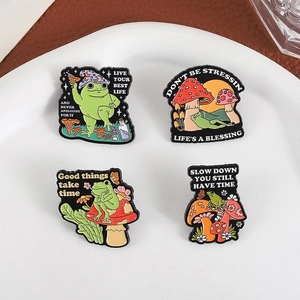 Lot de pins émaillés grenouille et champignon avec citations sur une assiette blanche