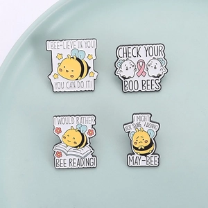 Set of 4 cute enamel bee pins with motivational English puns on a green tray