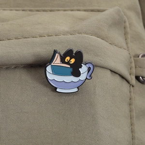 Detailed close-up of a cute black cat in a teacup enamel pin on a canvas backpack