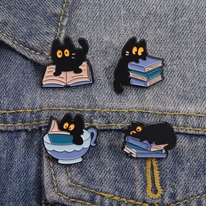 Set of four cartoon black cat enamel pins on denim, featuring cute cats reading books