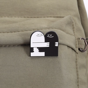 Détail des pin's émaillés fantômes noir et blanc s'enlaçant sur un sac en toile vert