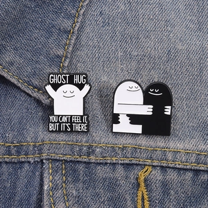 Detail of cute ghost enamel pins with Ghost Hug text on blue denim fabric background