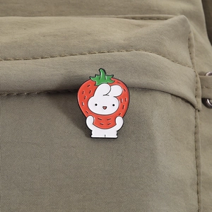 Close-up of a cute white rabbit in a strawberry suit enamel pin on a green canvas backpack