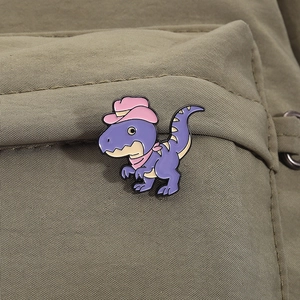 Detailed view of a purple dinosaur enamel pin with a cowboy hat on a canvas bag