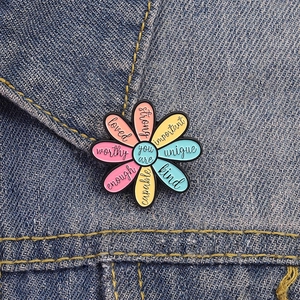 Colorful floral enamel brooch with motivational text on blue denim fabric background
