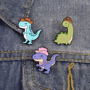 Set of three cute cartoon dinosaur enamel pins with cowboy hats on denim fabric