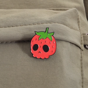 Detail of creative strawberry skull enamel pin pinned on a green canvas backpack pocket