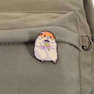 Detailed close-up of a cute metal hamster enamel pin on a green canvas bag texture