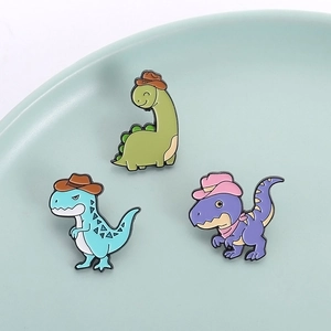 Three cute cartoon dinosaur enamel pins with cowboy hats on a ceramic plate for bags