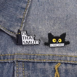 Dettaglio di spillette in smalto gatto nero con testo su giacca di denim blu