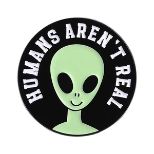 Close-up of a round enamel alien pin with Humans Aren't Real slogan for bags
