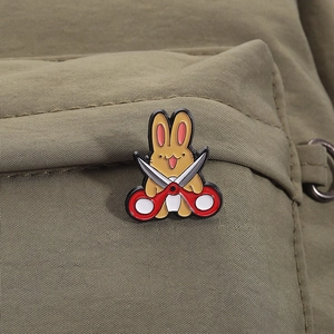 Close-up of a cute yellow bunny enamel pin with red scissors on a green canvas bag
