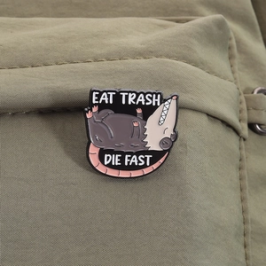 Detail van Eat Trash Die Fast opossum emaille speld op een groene nylon rugzakstof