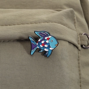 Macro shot of tropical fish enamel brooch with blue scales pinned on green canvas