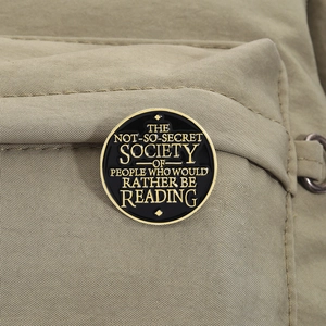 Close-up of circular black and gold enamel book lover pin on canvas bag texture