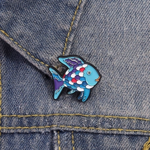 Detail of colorful enamel fish brooch pinned on premium blue denim fabric background