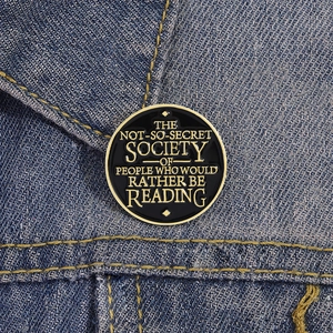 Détail d'un pin's rond en émail noir et or sur denim avec citation inspirante pour lecteurs