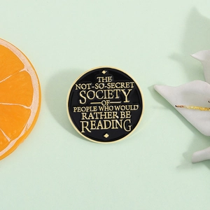 Enamel pin brooch featuring reading quote gold lettering on black metal background