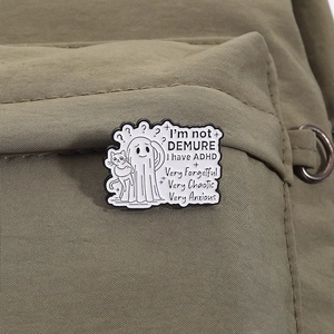 Close-up of a white enamel ghost and cat ADHD pin badge on a canvas fabric background