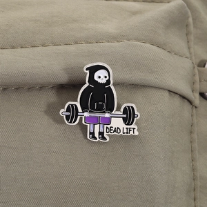 Detailed view of cartoon Grim Reaper enamel pin doing a deadlift on khaki canvas fabric