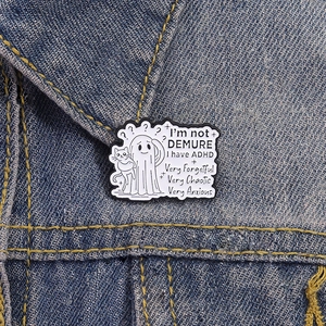Cartoon ghost and cat enamel pin featuring ADHD humor on a blue denim jacket