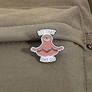 Detail of sloth meditation enamel pin on green fabric with Let That Shit Go text